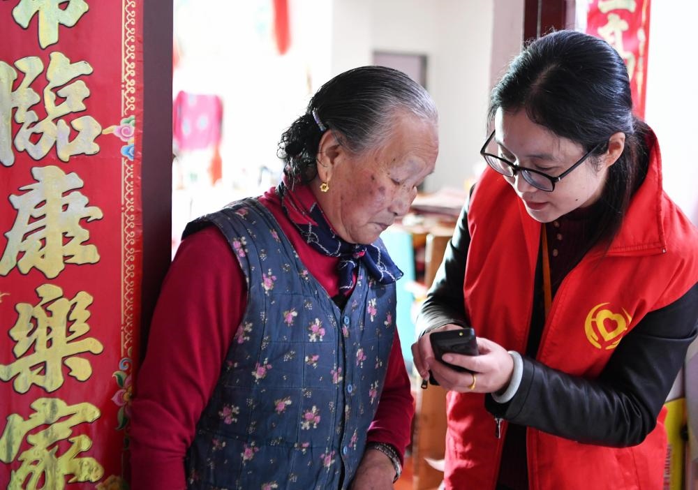 在福州市長樂區(qū)航城街道籌岐村，智慧養(yǎng)老平臺派駐社區(qū)的助老員（右）在為老人陳鳳英（左）講解養(yǎng)老定制手機的用法（2021年11月26日攝）。新華社記者 魏培全 攝