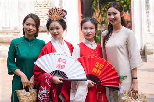 身穿古裝的中國游客和身穿越南傳統(tǒng)服飾奧黛的越南青年在文廟門前合影。