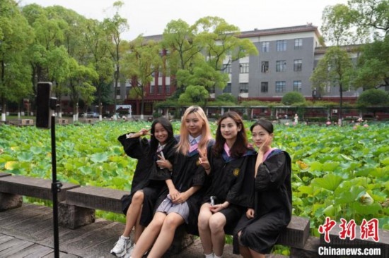 6月19日，時(shí)值一年畢業(yè)季，四川大學(xué)望江校區(qū)荷花池里的荷花盛開(kāi)，成為了畢業(yè)生們的打卡圣地，吸引了眾多畢業(yè)生拍照留念。圖為畢業(yè)生在荷花池邊拍照留念。中新社記者 安源 攝