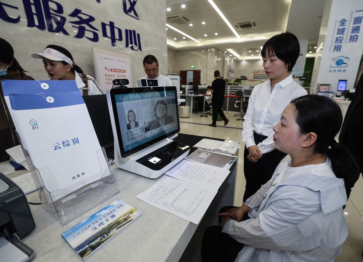 在浙江省嘉興市秀洲區(qū)王江涇鎮(zhèn)便民服務(wù)中心的“跨域通辦·云綜窗”窗口，辦理開業(yè)登記的個(gè)體工商戶（右一）通過該系統(tǒng)與江蘇省蘇州市吳江區(qū)盛澤鎮(zhèn)行政審批局工作人員視頻連線，進(jìn)行身份讀取及材料線上審核（2024年5月9日攝）。新華社記者 徐昱 攝