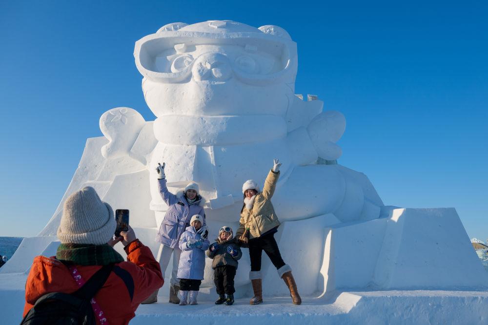2025年1月3日，在黑龍江哈爾濱冰雪大世界園區(qū)，游客與亞冬會吉祥物雪雕“濱濱”合影